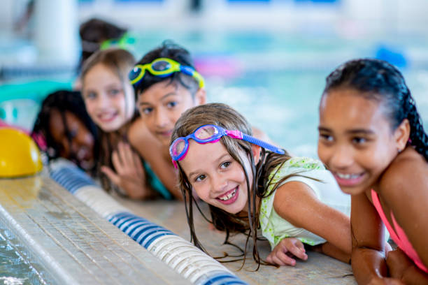 Poolside A multi-ethnic group of kids are indoors in a pool. Some of them are wearing goggles and smiling at the camera. leisure activity stock pictures, royalty-free photos & images