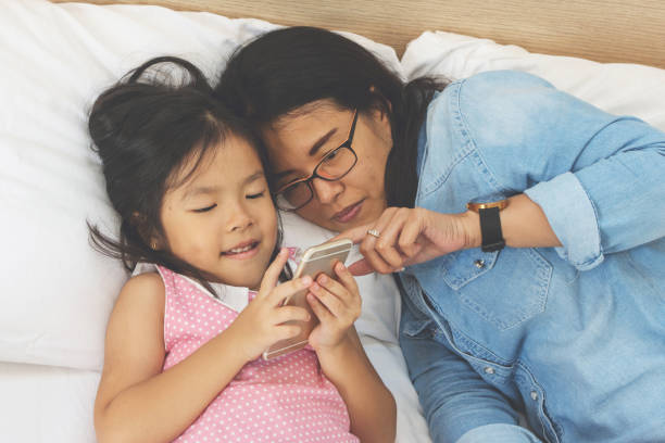 istock young mom and her little daughter are using a smartphone on bed at home 1009344566