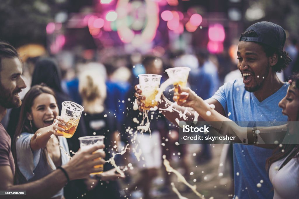Group of cheerful friends having fun with beer on a music concert. Young happy friends having fun while toasting and spilling beer on a music festival. Beer - Alcohol Stock Photo