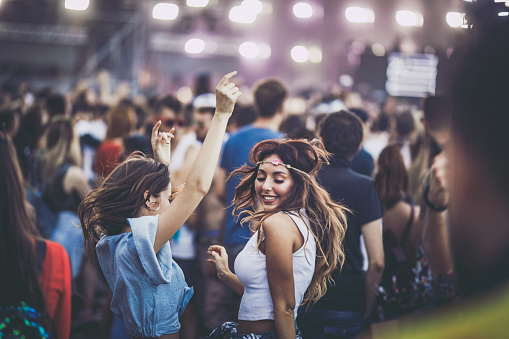 Young happy female friends having fun while dancing on a music concert.
