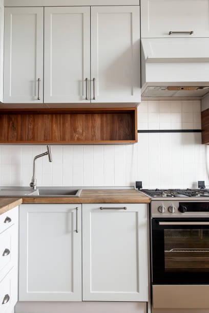 istock Stylish light gray kitchen interior with modern cabinets and stainless steel appliances. kitchen design in scandinavian style. hardwood floor and wooden worktop, granite sink and stylish faucet 1009379458