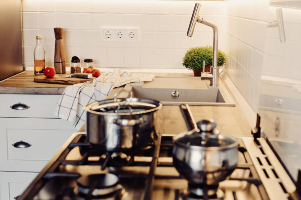 istock Cooking on Modern Kitchen  in scandinavian style. stylish kitchen interior with modern furniture and stainless steel appliances. wooden countertop, steel stove, board,knife and spices, tomatoes 1009379532
