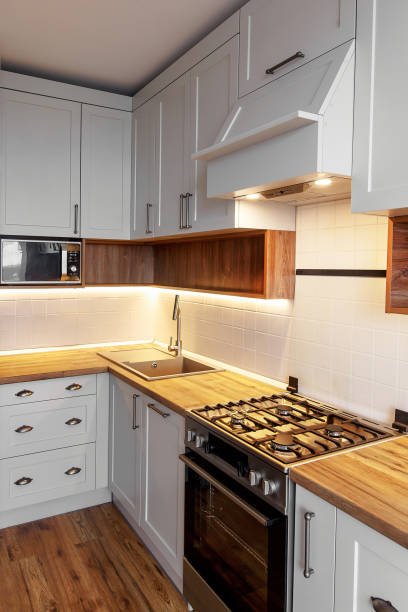 istock Stylish light gray kitchen interior with modern cabinets with light and stainless steel appliances. kitchen design in scandinavian style. contemporary cooker, wooden worktop and chimney 1009379558
