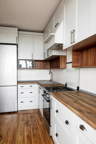 istock Stylish light gray kitchen interior with modern cabinets and stainless steel appliances. kitchen design in scandinavian style. hardwood floor and wooden worktop, granite sink and stylish faucet 1009379582