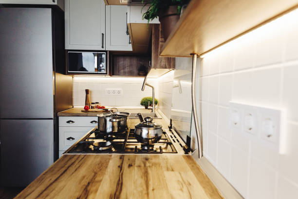 istock Cooking on Modern Kitchen  in scandinavian style. stylish kitchen interior with modern furniture and stainless steel appliances. wooden countertop, steel stove, board,knife and spices, tomatoes 1009383694