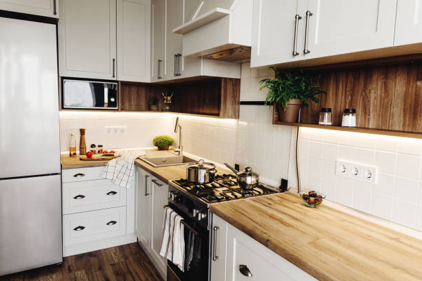 istock Cooking on Modern Kitchen  in scandinavian style. stylish kitchen interior with modern furniture and stainless steel appliances. wooden countertop, steel stove, board,knife and spices, tomatoes 1009383704