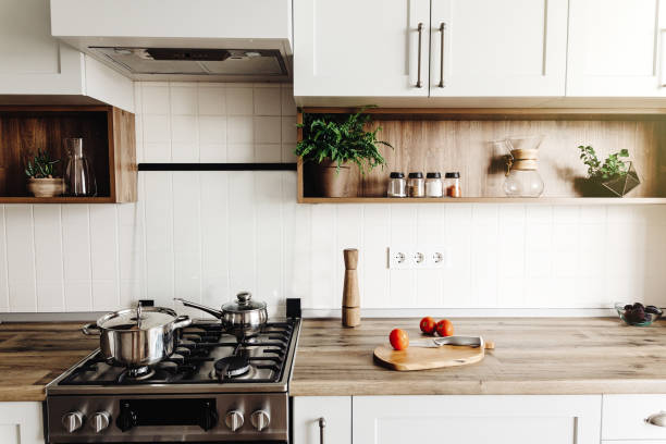 istock Cooking on Modern Kitchen  in scandinavian style. stylish kitchen interior with modern furniture and stainless steel appliances. wooden countertop, steel stove, board,knife and spices, tomatoes 1009383840