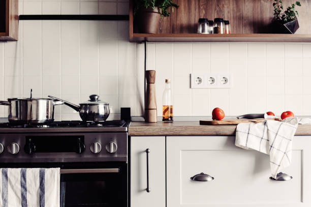 istock Cooking on Modern Kitchen  in scandinavian style. stylish kitchen interior with modern furniture and stainless steel appliances. wooden countertop, steel stove, board,knife and spices, tomatoes 1009384024