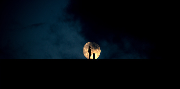 Silhouette of woman and border collie against blood moon rising behind hill