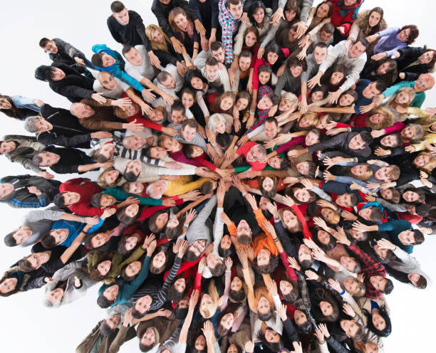 Above view of happy group of people joining hands in unity. High angle view of large group of happy mixed-age people standing and joining their hands while looking at the camera. Isolated on white. sea of hands stock pictures, royalty-free photos & images