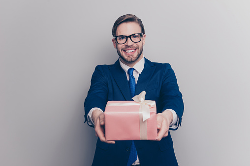 International women's day concept. Portrait of funny funky cute handsome lovely modern stylish guy giving you big pink present box stretching in hands isolated on gray background copy-space