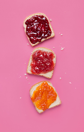 Toast slices with fruit jam on a pink background viewed from above. Selection of bread slices with fruit marmalade. Top view