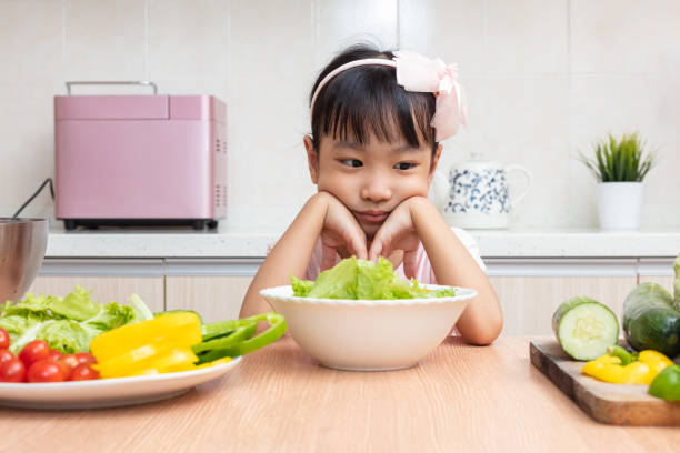 Asian Chinese little girl eating salad in the kitchen Asian Chinese little girl eating salad in the kitchen at home obsessive stock pictures, royalty-free photos & images