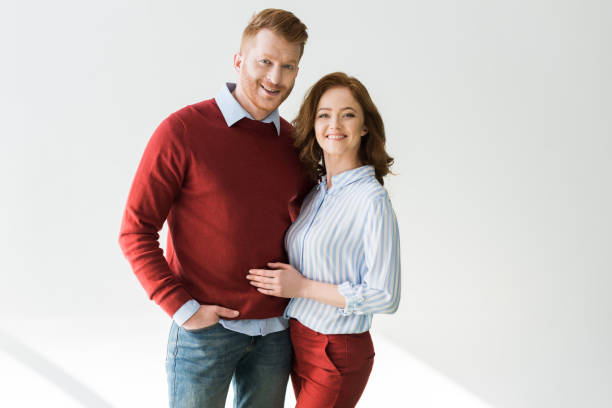 istock cheerful red haired couple standing together and smiling at camera on grey 1009456734
