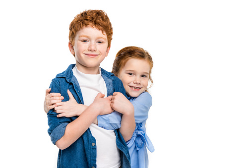 Couple of charming childs having fun outdoors. Portrait of beautiful girl and boy are hugging, smiling and looking at the camera. Little brother and sister in park on a green grass.