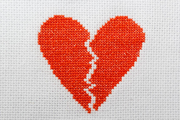 istock The broken heart is embroidered with red threads on a white cloth. 1009468718