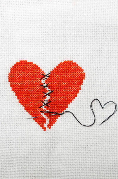 istock The broken heart is embroidered with red threads on a white cloth. 1009468720
