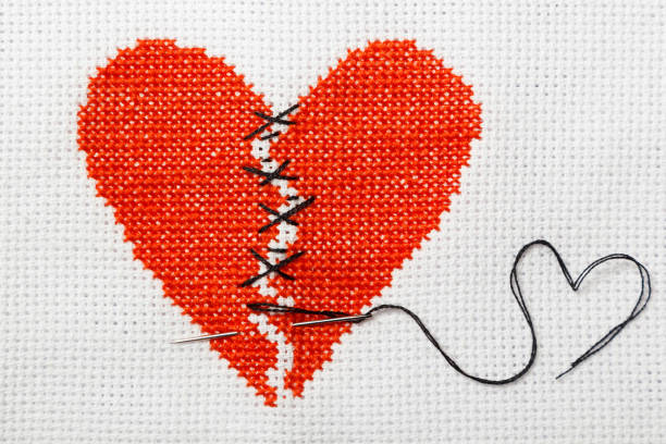 istock The broken heart is embroidered with red threads on a white cloth. 1009468722
