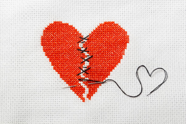 istock The broken heart is embroidered with red threads on a white cloth. 1009468724