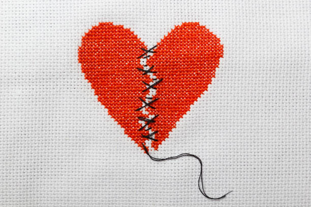 istock The broken heart is embroidered with red threads on a white cloth. 1009468754