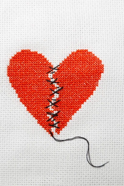 istock The broken heart is embroidered with red threads on a white cloth. 1009468758