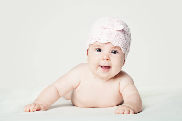 istock Smiling baby in pink hat lying on white blanket 1009468788
