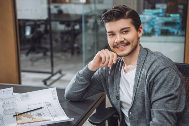 istock handsome young architect sitting at workplace with building plans at office 1009474466