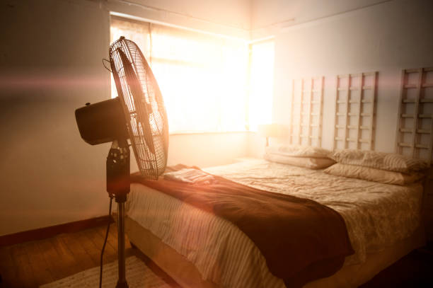 Electric fan next to bed with sunshine coming through the window. stock photo