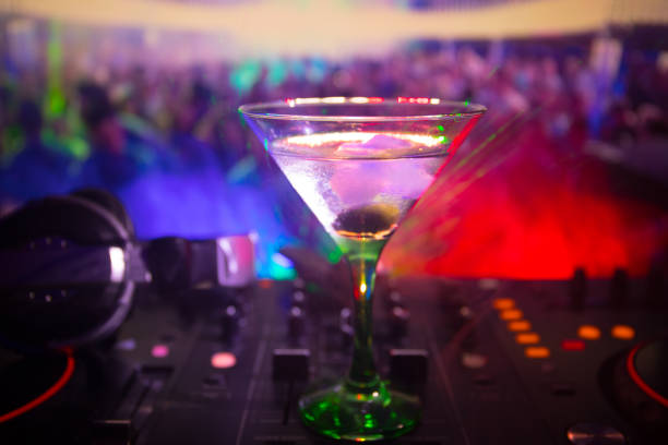 istock Glass with martini with olive inside on dj controller in night club. Dj Console with club drink at music party in nightclub with disco lights. Close up view 1009487072