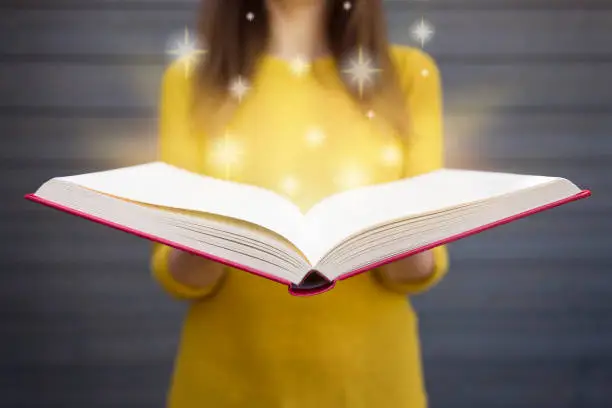 Photo of Light coming from book in woman's hands. Concept of wisdom, religion, reading, imagination, knowledge