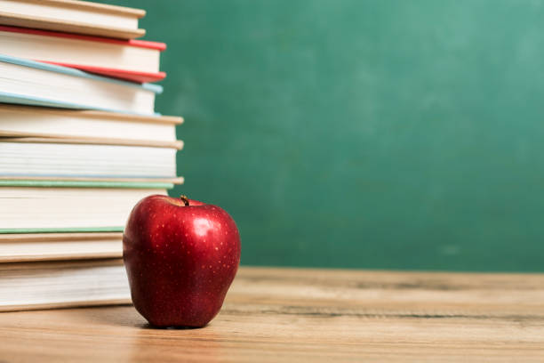 istock Textbooks, apple on wooden school desk with chalkboard. 1009497578