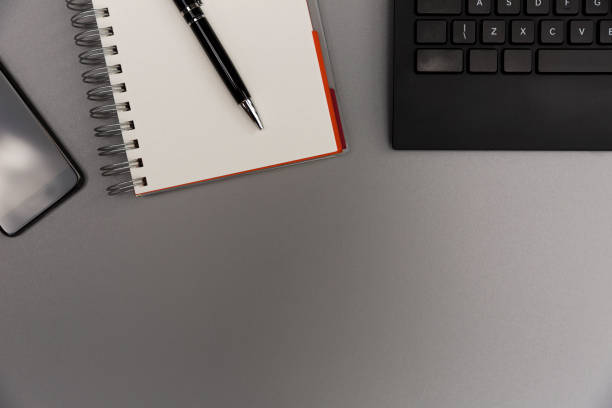 istock Modern grey office desk table with smartphone, blank notebook page with pen and keyboard. Working, writing concept 1009498494