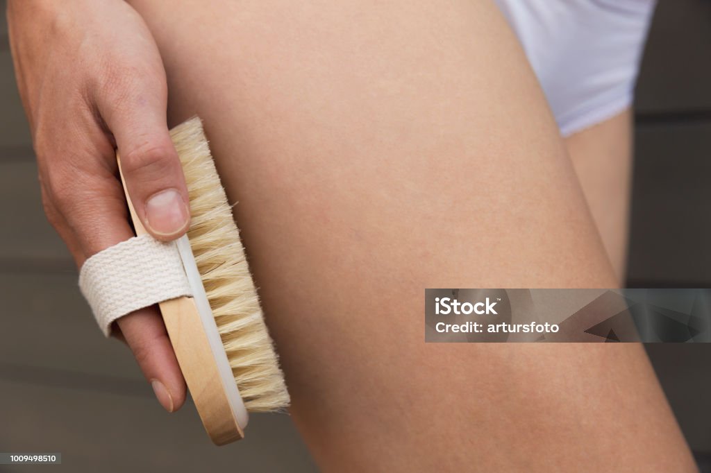 Woman's arm holding dry brush to top of her leg. Cellulite treatment, dry brushing Brushing Stock Photo