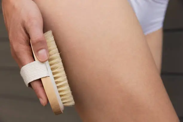 Woman's arm holding dry brush to top of her leg. Cellulite treatment, dry brushing