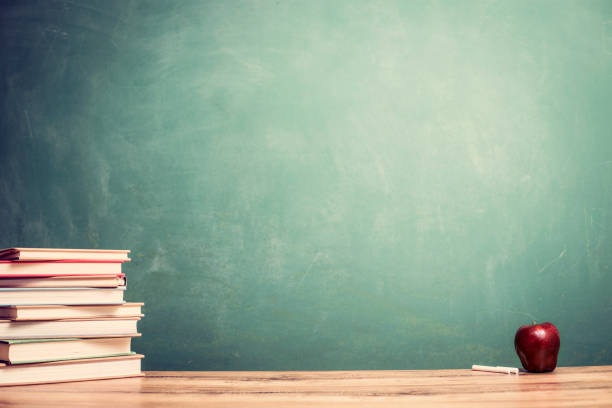istock Textbooks, apple on wooden school desk with chalkboard. 1009498524