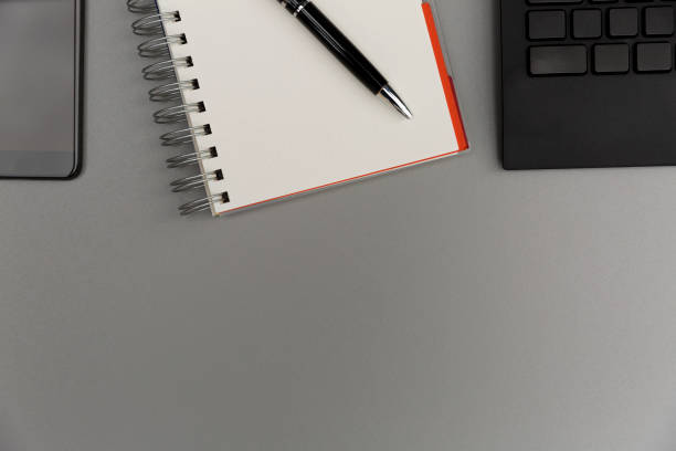 istock Modern grey office desk table with smartphone, blank notebook page with pen and keyboard. Working, writing concept 1009498550