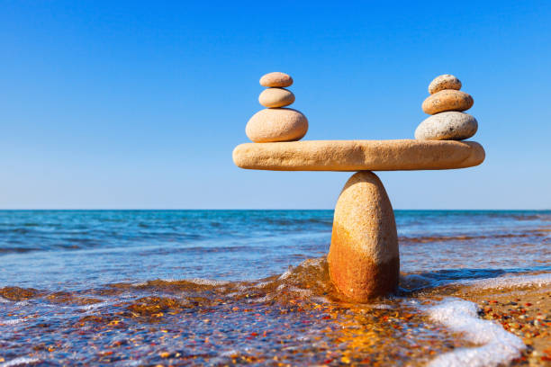 symbolic scales of the stones, illuminated by the evening sun, against the sea, close-up. pros and cons concept - balance simplicity nature beach imagens e fotografias de stock