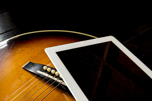 The never ending process of learning.  Here we see an acoustic guitar and a digital tablet.  The scene that someone is learning or practicing a new skill, with the help of the internet, or online tutorials.  Studio shot.
