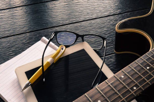 The never ending process of learning.  Here we see an acoustic guitar, a digital tablet and a pair of glasses.  The scene that someone is learning or practicing a new skill, with the help of the internet, or online tutorials.  Studio shot.