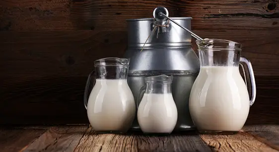 A jug of milk and glass of milk on a wooden table