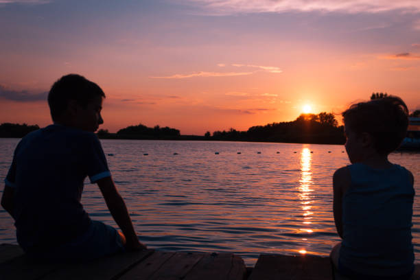 istock Two boys relaxing on a pier at sunset. 1009529978