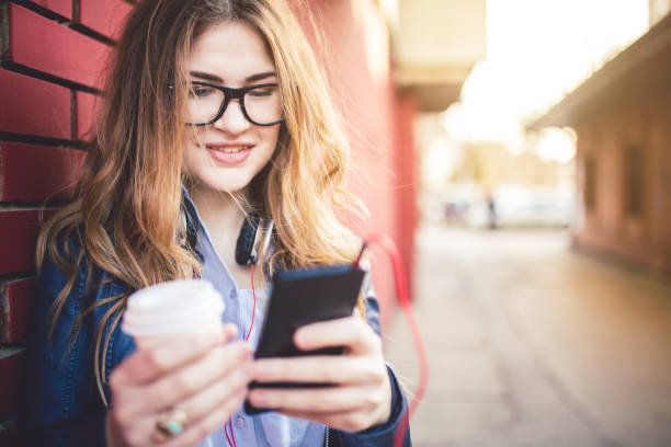 istock Woman standing in front of brick wall typing a text message and enjoying in coffee. 1009538542