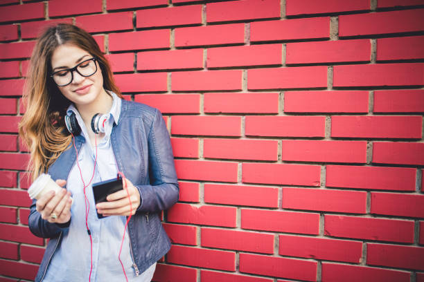 istock Woman standing in front of brick wall typing a text message and enjoying in coffee. 1009541008