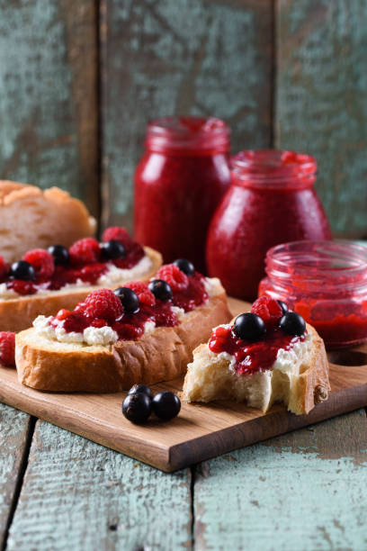 istock Homemade jam on toasts. Raspberry jam, ricotta and raw berries on ciabatta bread on blue background 1009544616