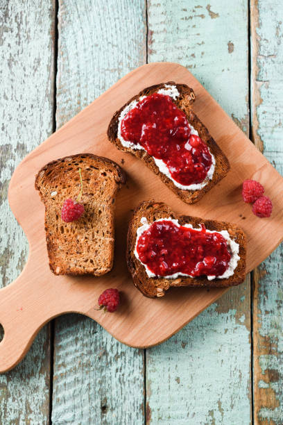 istock Healthy breakfast, jam on toasts. Raspberry jam, ricotta and raw berries on rye bread on blue background 1009546730