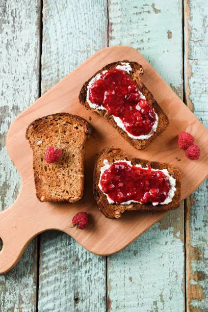 Healthy breakfast, jam on toasts. Raspberry jam, ricotta and raw berries on rye bread on blue background above view