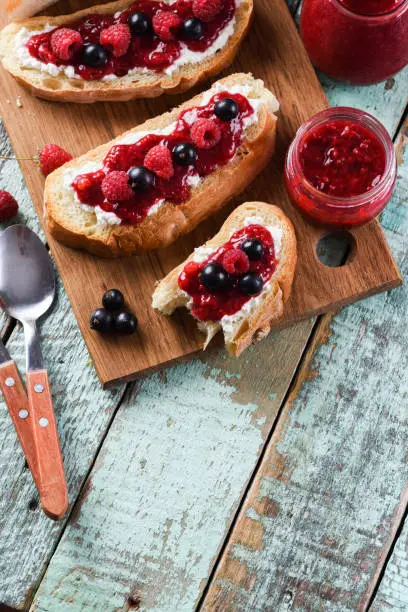 Healthy snack, jam on toasts. Raspberry jam, ricotta and raw berries on ciabatta bread on rustic blue background above view copyspace