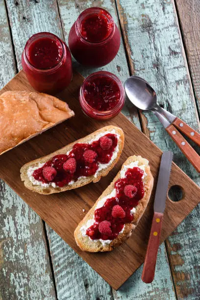 Healthy snack. Raspberry jam, ricotta and raw berries on ciabatta bread on blue background above view
