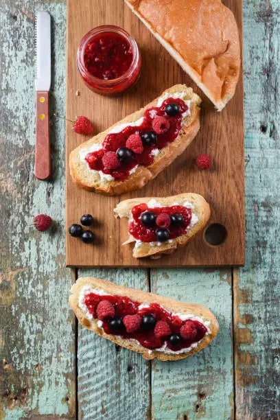 Quick breakfast, jam on toast. Raspberry jam, ricotta and raw berries on ciabatta bread on blue background above view