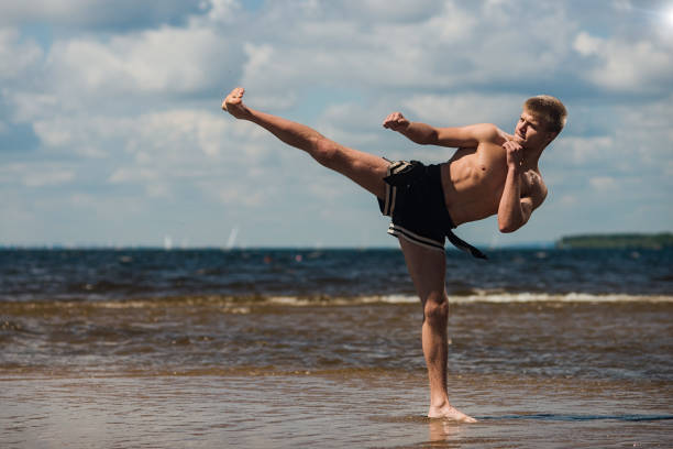 kickboxer tritt unter freiem himmel im sommer gegen das meer. - wushu action aggression power stock-fotos und bilder
